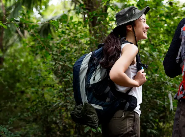 Woman with a wide-brimmed hat and a backpack hiking in the tropical rainforest.